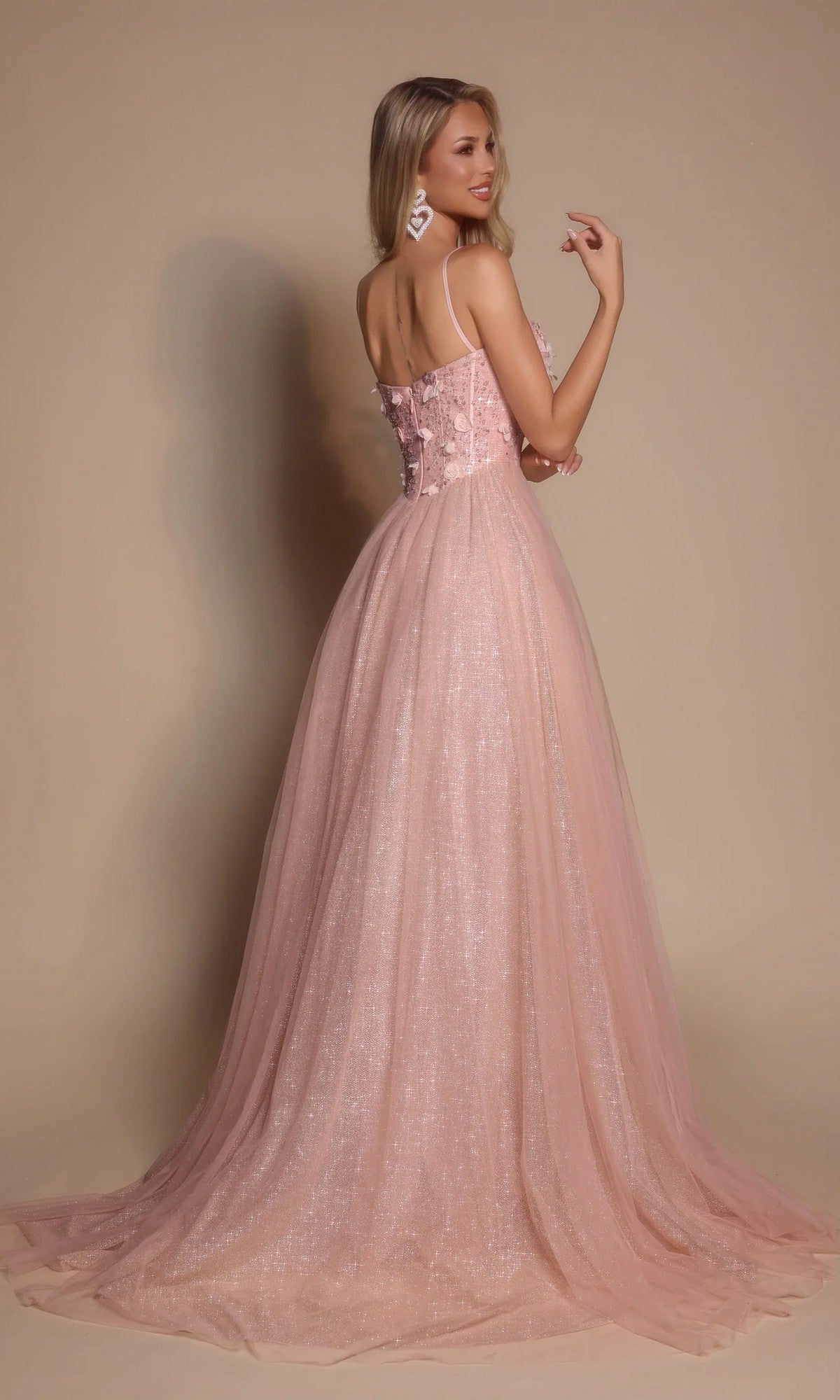 Woman wearing the Portia and Scarlett PS26146 Glitter Prom Ball Gown, featuring a blush pink fitted boned-corset bodice and a flowing shimmery skirt, poses against a plain beige background.